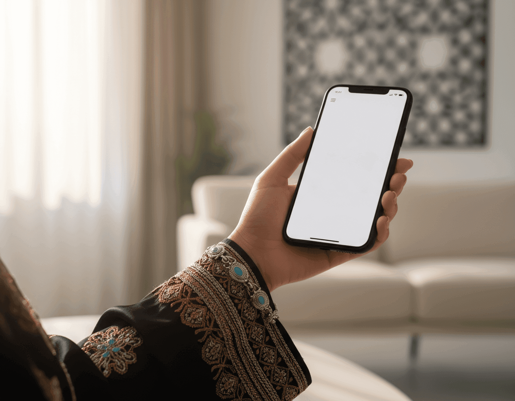 A hand adorned with traditional embroidery holding a smartphone with a blank white screen.